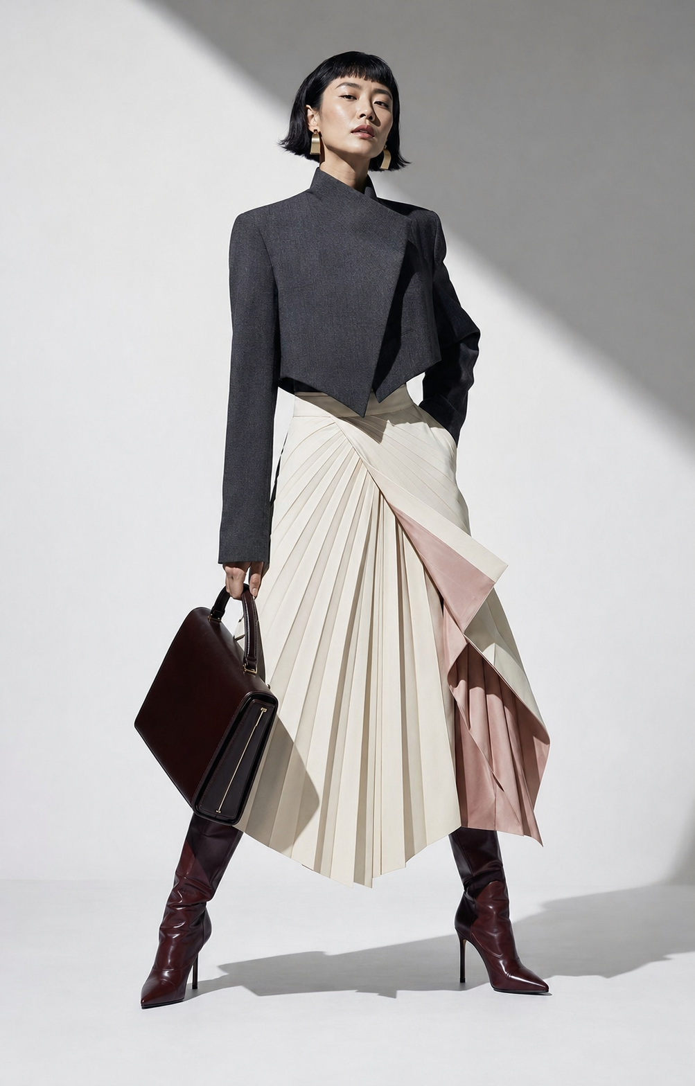 Woman in architectural charcoal tailoring and a pleated ivory skirt